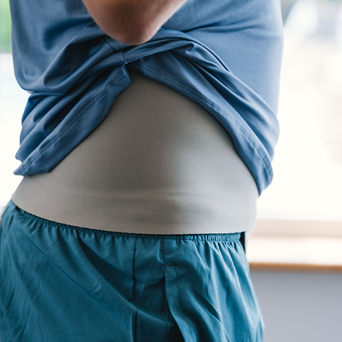 En man tränar på gym med sin stomi och sitt stomibälte med ficka i grå färg